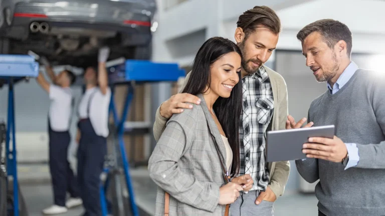 Mid adult manager and young couple using touchpad in auto repair shop